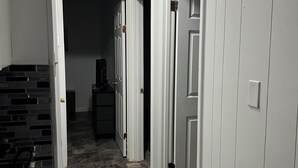 A hallway with white walls, a patterned floor, and a door leading to a dark room.