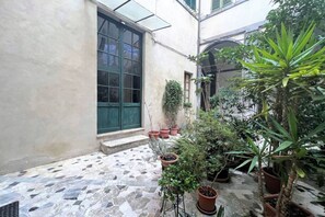 A courtyard with a tiled floor, potted plants, and a large window with green shutters. - CASA CONTI – near Piazza del Campo (Siena)
