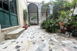 A courtyard with a tiled floor, potted plants, and a green door. - CASA CONTI – near Piazza del Campo (Siena)