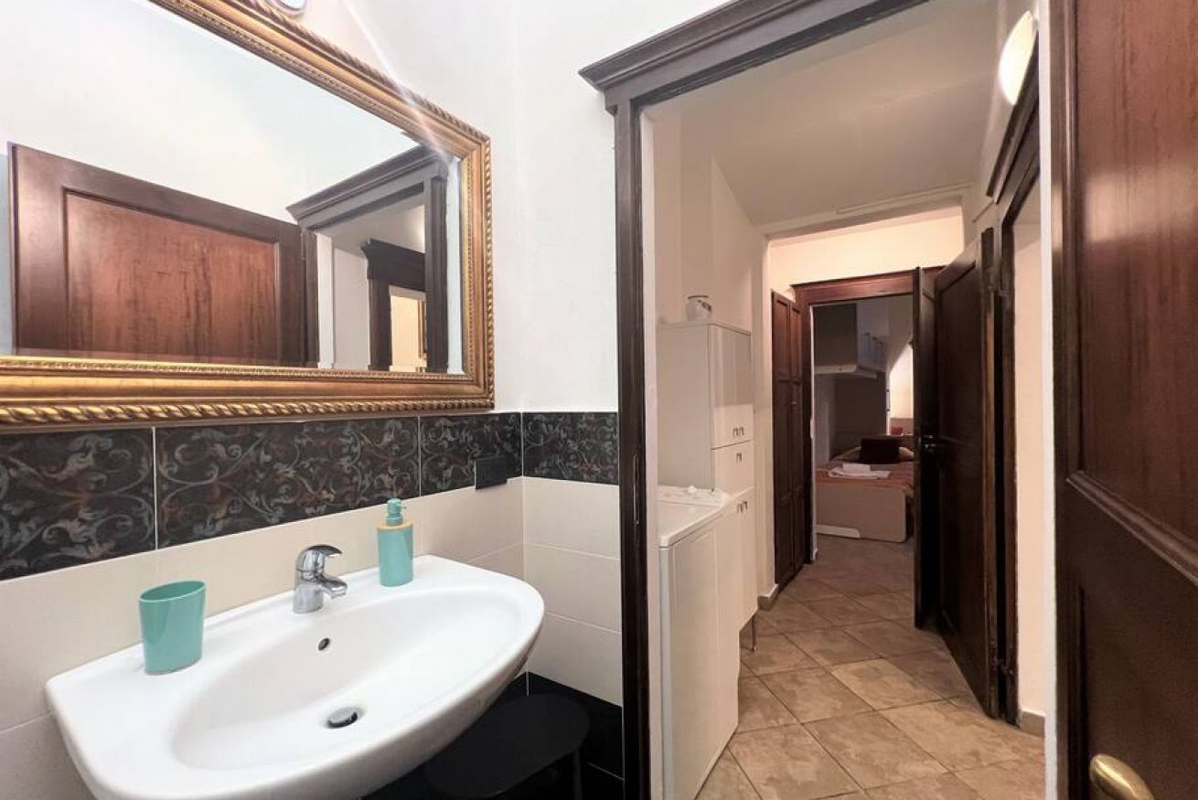 Une salle de bain avec un lavabo blanc, un miroir et une porte en bois foncé.
