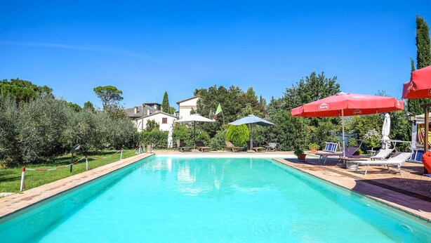 A swimming pool with lounge chairs and umbrellas, surrounded by greenery and buildings. - Nice home in Spoleto with kitchen (Spoleto)