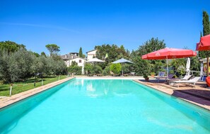 A swimming pool with lounge chairs and umbrellas, surrounded by greenery and buildings. - Nice home in Spoleto with kitchen (Spoleto)