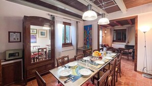A dining area with a long table set for four, surrounded by wooden chairs. There is a large window with curtains, a painting on the wall, and a door leading to another room. - Nice home in Spoleto with kitchen (Spoleto)