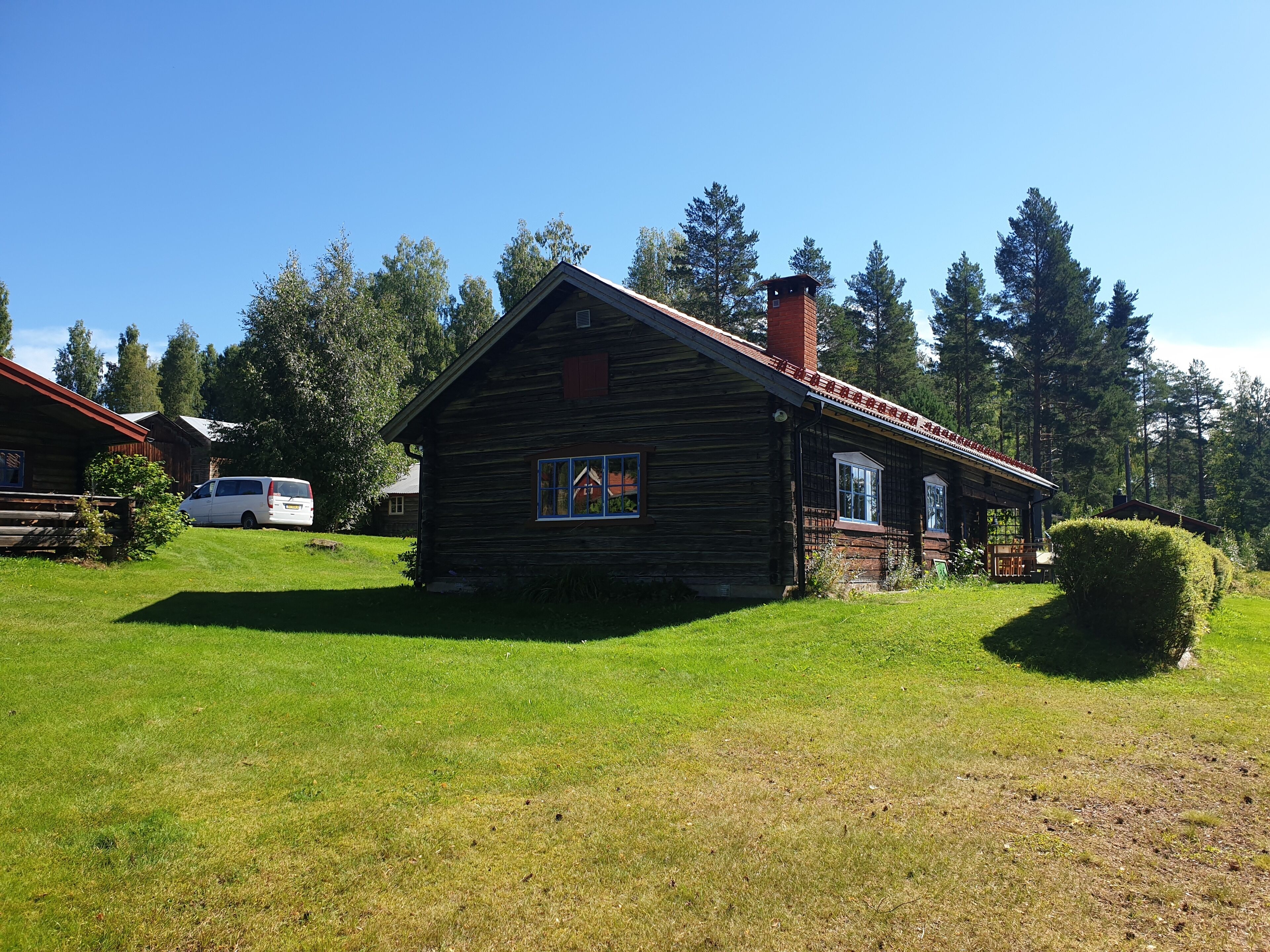 Eine rustikale Holzhütte mit rotem Dach, umgeben von üppigem Grün und hohen Bäumen.