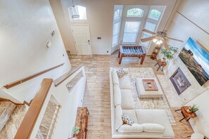 A spacious living area with a sofa, coffee table, and a foosball table. There is a staircase with a railing, a ceiling fan, and a door. - Spacious Northeast El Paso home near Franklin Mountains, Fort Bliss & Meta site. (El Paso)