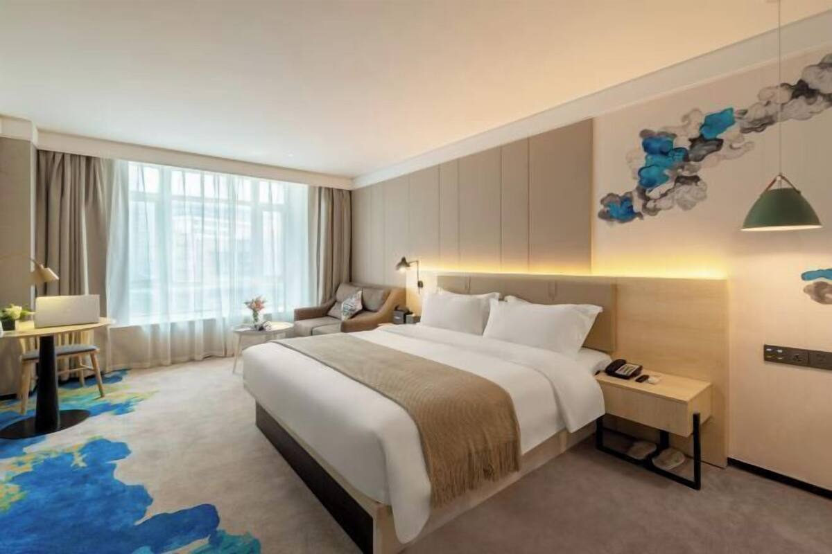 Een moderne hotelkamer met een groot bed, een bureau, een stoel, een klein tafeltje en een decoratief object aan de muur.