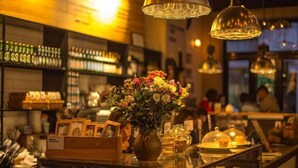 Un interior de cafetería con una vitrina de vidrio, un jarrón de flores y estantes con frascos y recipientes.