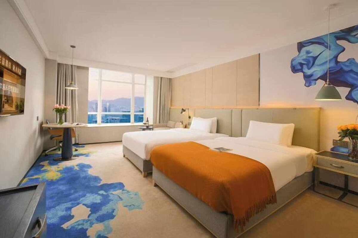 Hotelkamer met twee bedden, een bureau, een stoel, een raam met uitzicht op de stad en een groot abstract schilderij.