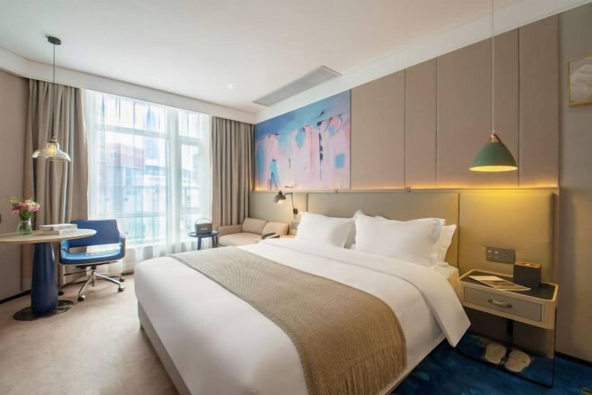 Een hotelkamer met een bed, een bureau, een stoel, een nachtkastje en een groot raam.