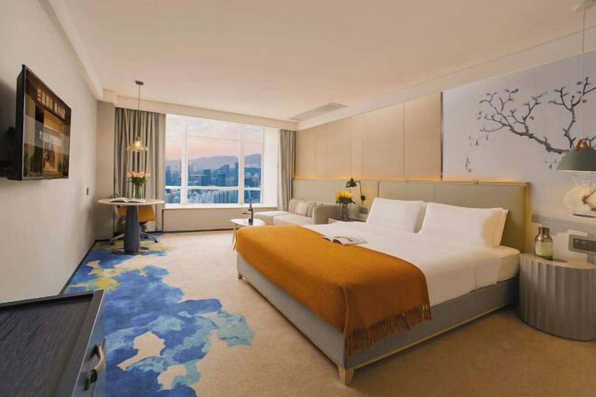 Hotelkamer met een groot bed, een bureau, een stoel, een raam met uitzicht op de stad, en een schilderij aan de muur.