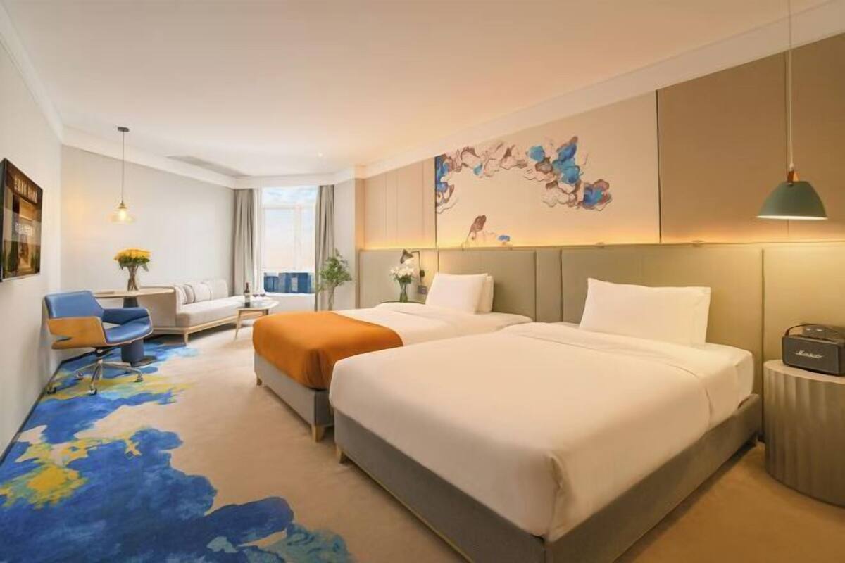 Een hotelkamer met twee bedden, een bureau, een stoel, een lamp en een schilderij aan de muur.