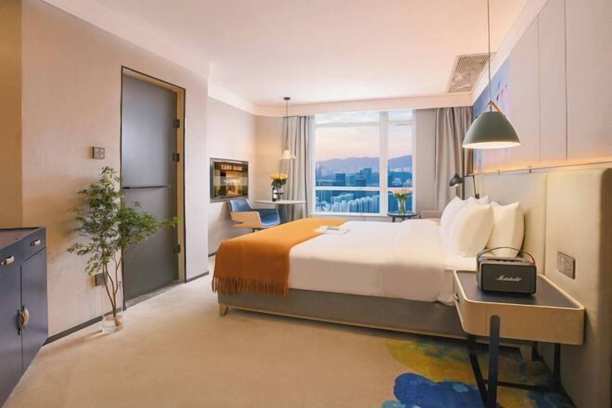 Een hotelkamer met een bed, nachtkastje, lamp en uitzicht op de stad.