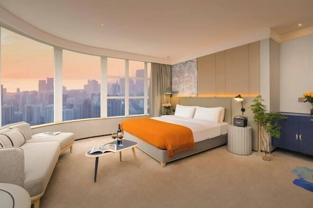 Een moderne hotelkamer met een groot raam, een bed, een slaapbank, een kleine tafel en een kast.