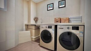 Un lavadero con dos lavadoras de carga frontal, un lavabo y una pequeña estantería con objetos decorativos.