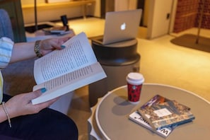 A person reading a book at a table with a laptop and a coffee cup nearby.