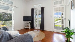 A spacious living room with a large TV, a round rug, and a balcony with a view of the city. - Family Home in Balmoral - Family Stays (Balmoral)