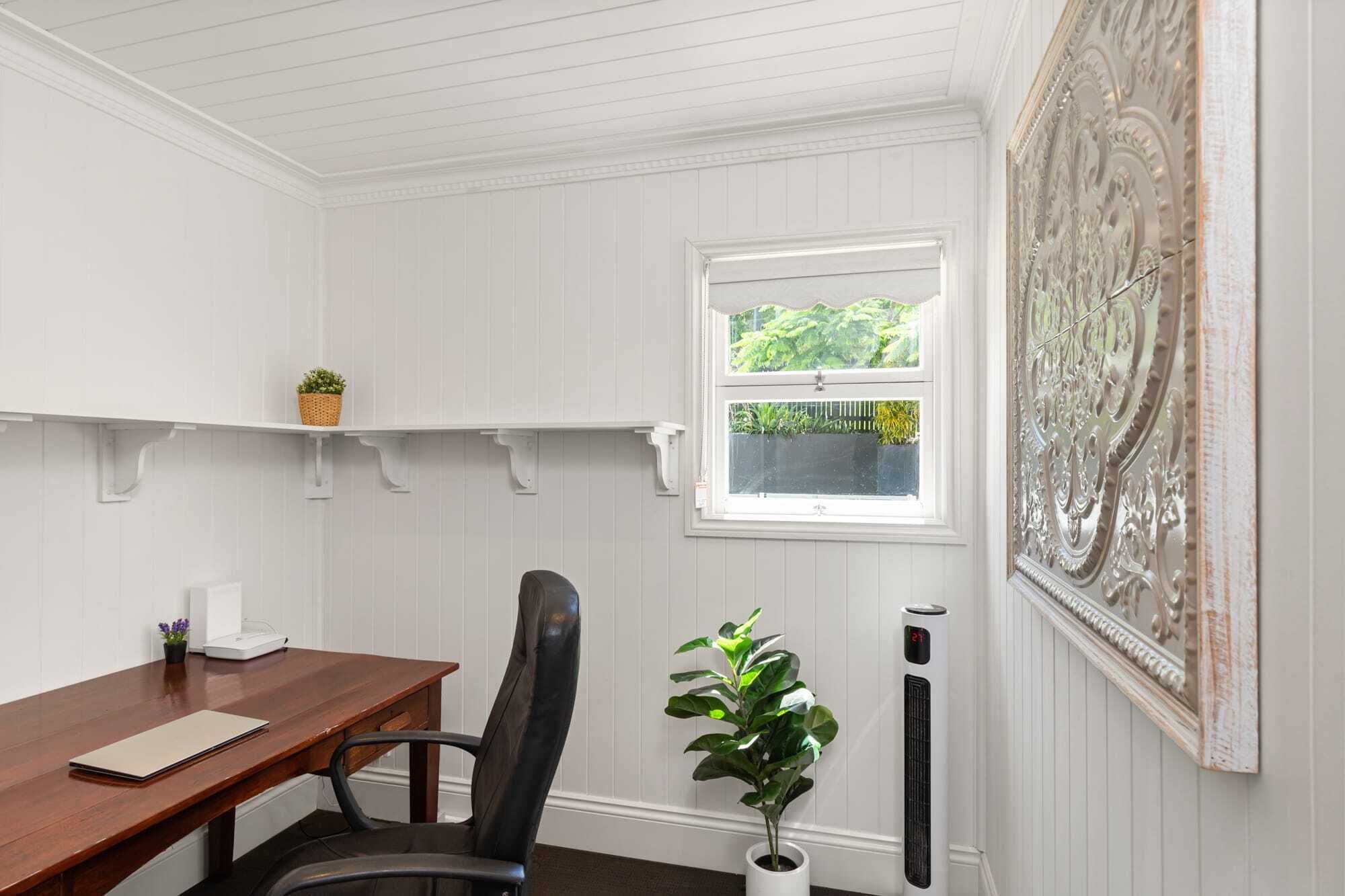 Une pièce comprenant un bureau en bois, une chaise, une plante en pot, un radiateur et une fenêtre donnant sur un paysage verdoyant.