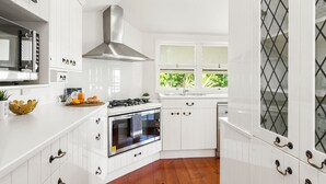 A modern kitchen with white cabinetry, stainless steel appliances, and a window with a view of greenery. - Family Home in Balmoral - Family Stays (Balmoral)