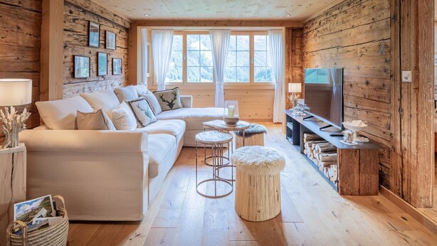 A cozy cabin interior with a sofa, ottoman, TV, and wooden walls. - Chalet Bijou+ 1 OG by Interhome (Lenk)