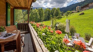 A wooden deck with a table and chairs, surrounded by blooming flowers. - Chalet Bijou+ 1 OG by Interhome (Lenk)