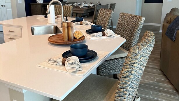 Een moderne keuken met een centraal eiland, een eethoek met stoelen en uitzicht op de woonkamer.