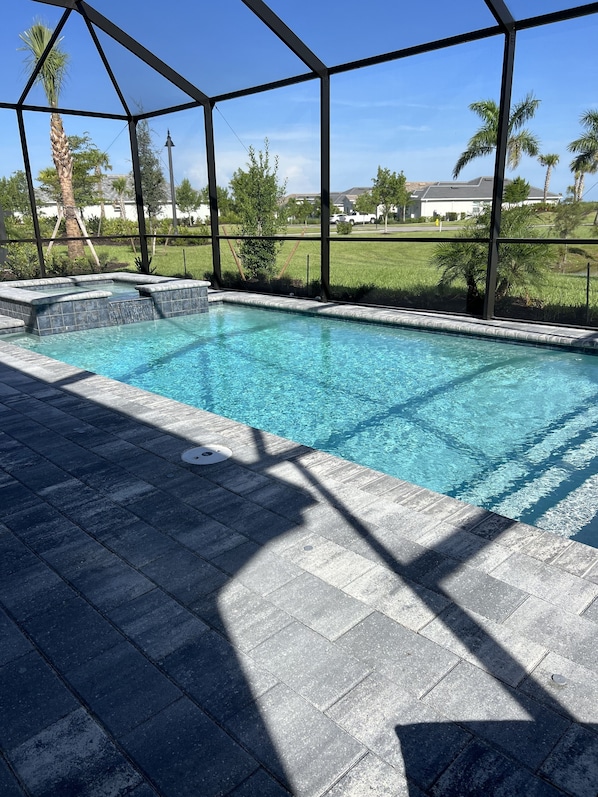Una piscina rectangular con superficie de agua azul cristalina, rodeada por una solana empedrada.