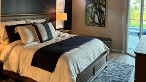 Een slaapkamer met een groot bed, nachtkastje, lamp, schilderij en uitzicht op het groen.