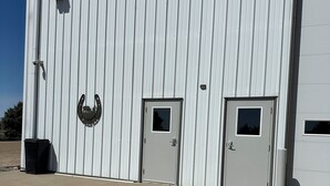 Un edifici industrial gran amb façana de metall ondulat, dues portes i una làmpada penjant.