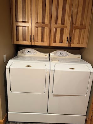 A laundry room with two stacked front-loading washing machines and wooden cabinets above.