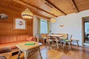 A wooden interior with a sofa, dining table, chairs, and a ceiling with wooden beams.