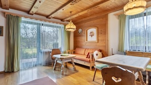 Un intérieur en bois comprenant un canapé, des fauteuils, une table et un plafond avec des poutres apparentes.