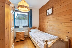 A wooden-paneled room with a bed, a nightstand, a lamp, and a window with curtains.