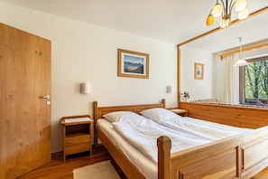 Un lit en bois avec une table de chevet, une armoire en bois, un miroir et une fenêtre donnant sur des arbres.