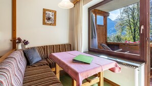Een gezellige kamer met een houten bankje, een tafel met een boek, een raam met uitzicht op bergen, en een lijst met een foto aan de muur.