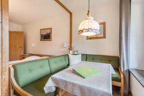 A room with a green upholstered bench, a table with a book, a hanging lamp, and framed pictures on the wall.