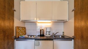Een kleine keuken met witte kastjes, een koffiezetapparaat en een gootsteen.