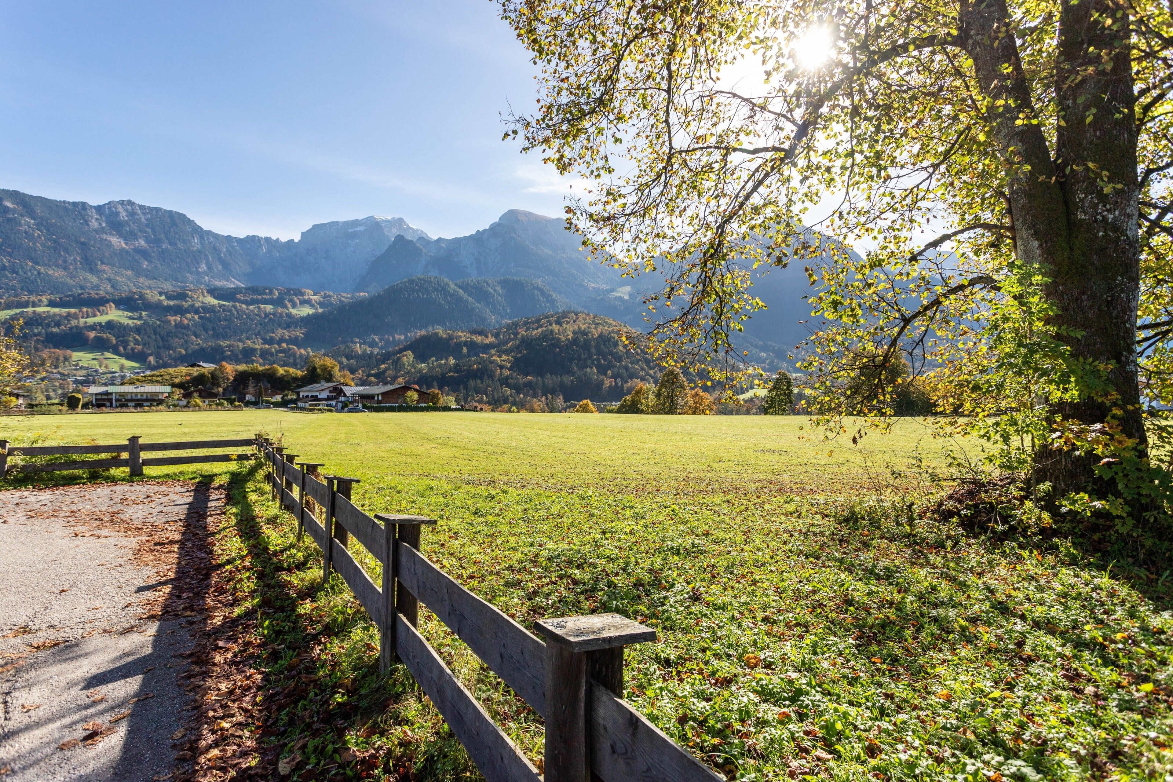 A rural landscape with a wooden fence, a clear sky, and mountains in the background.