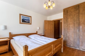 Une chambre à coucher avec un lit en bois, une table de chevet, une armoire et un luminaire fixé au plafond.