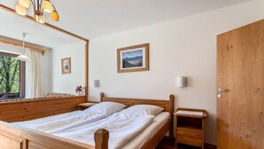 Een houten bed met witte lakens, een nachtkastje, een spiegel, een ingelijst beeld en een houten garderobe.