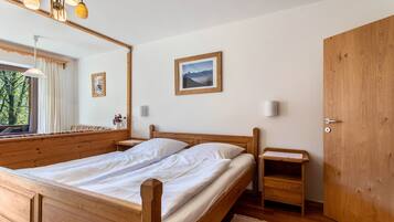 Een houten bed met witte lakens, een nachtkastje, een spiegel, een ingelijst beeld en een houten garderobe.