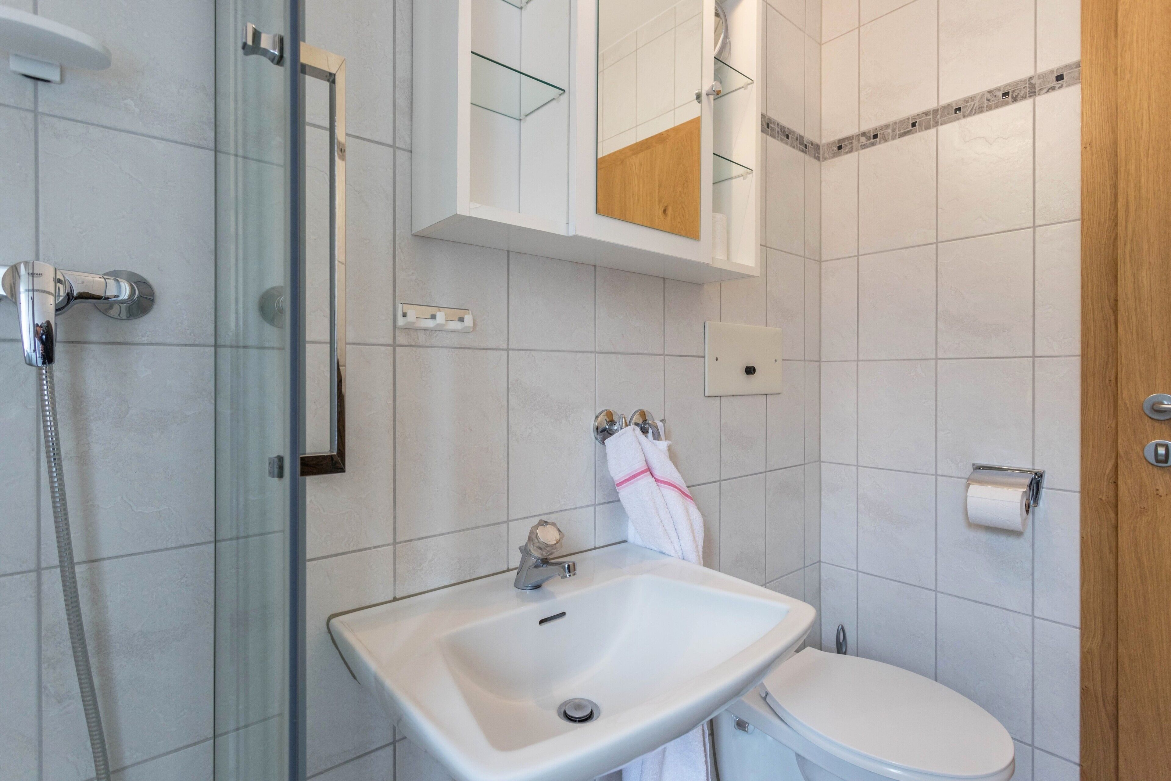 A bathroom with a glass shower enclosure, a white sink, a toilet, and a wooden cabinet above the sink.