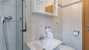 A bathroom with a glass shower enclosure, a white sink, a toilet, and a wooden cabinet above the sink.