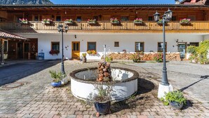 Ein Innenhof mit einem runden Brunnen, Blumentöpfen und einem Gebäude mit hölzernen Balkonen.