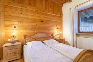 Quarto com painéis de madeira, duas camas, mesas de cabeceira e uma janela com cortinas.