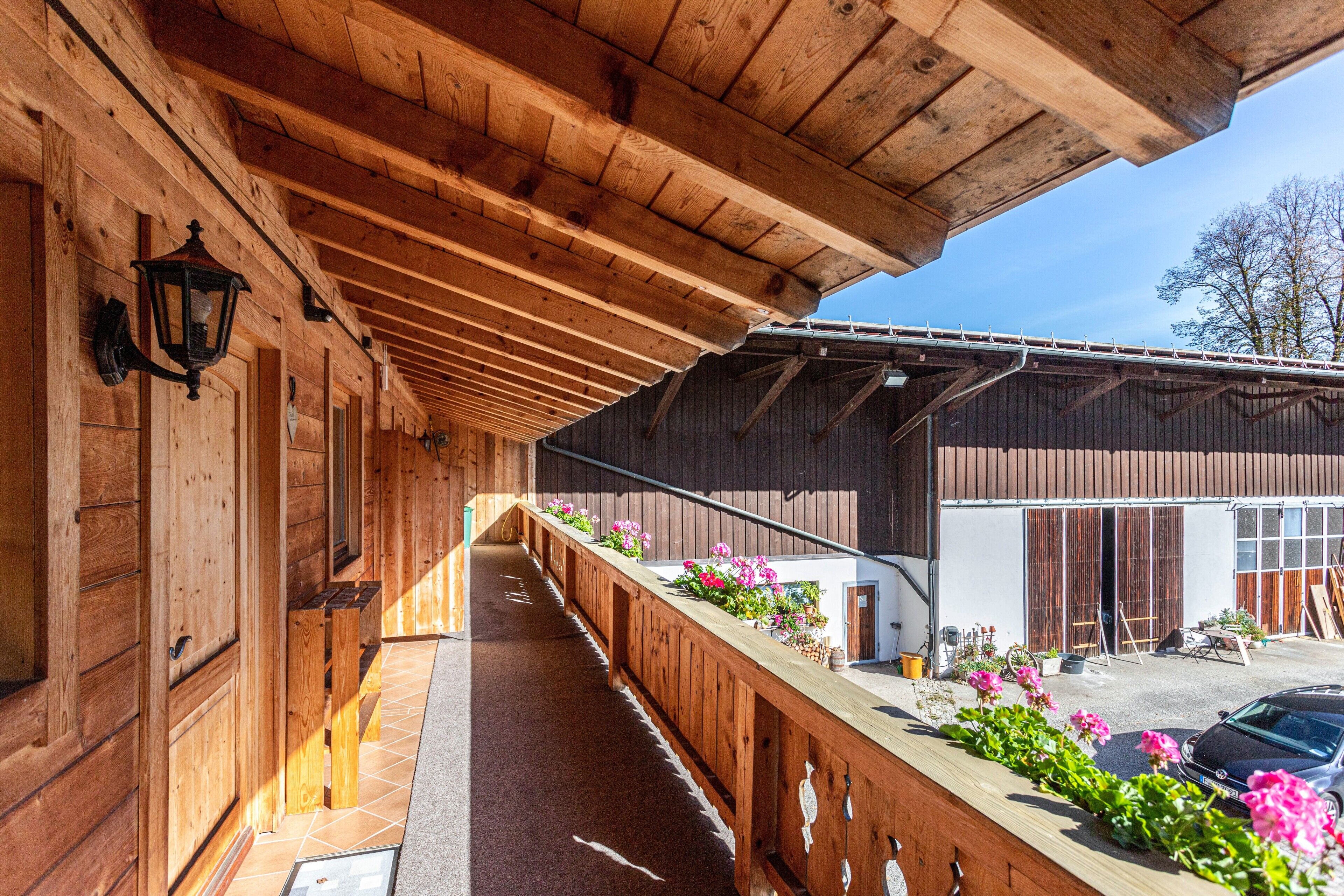 Une véranda en bois, dotée d’une balustrade en bois, un chemin et un bâtiment avec un garage en arrière-plan.