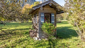Une cabane en bois rustique, dotée d’un toit en pente, d’un petit porche et d’une jardinière ornée de fleurs rouges.