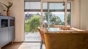 Een modern interieur met een schuifdeur naar een balkon, een eethoek met tafel en stoelen, en een grijze kast met decoratieve objecten.