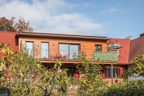 Un immeuble de deux étages doté d’un balcon, de grandes fenêtres et d’un toit rouge.