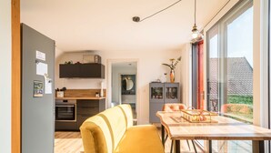 Een moderne keuken met houten kasten, een eethoek met gele stoelen en een groot raam met uitzicht op de omgeving.