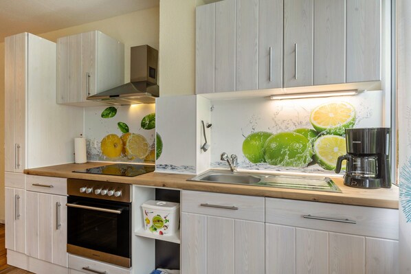A kitchen with white cabinets, a stainless steel sink, a coffee maker, and a wall decorated with citrus fruit illustrations.